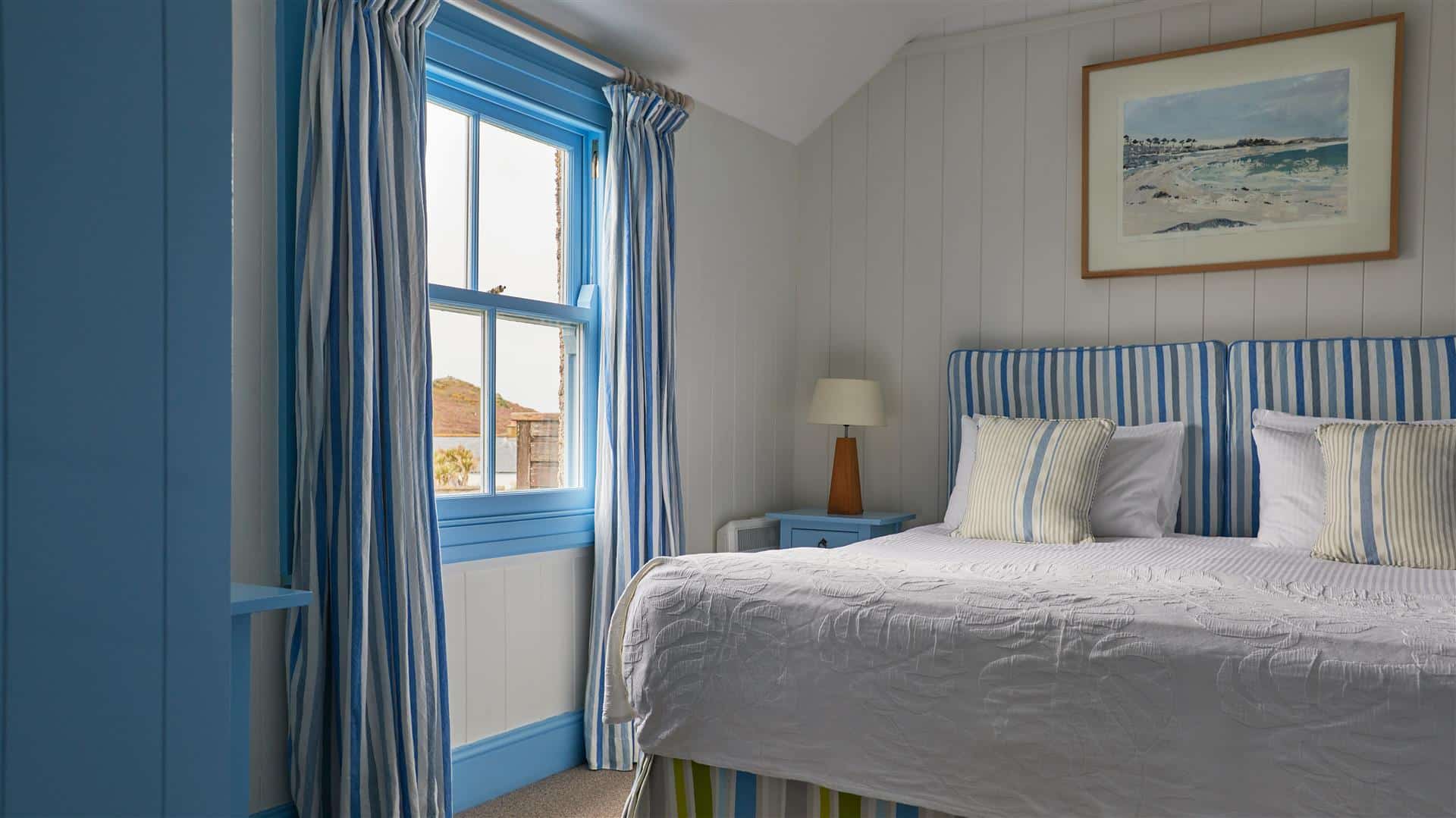 A hotel bedroom with king size bed and blue striped soft furnishings
