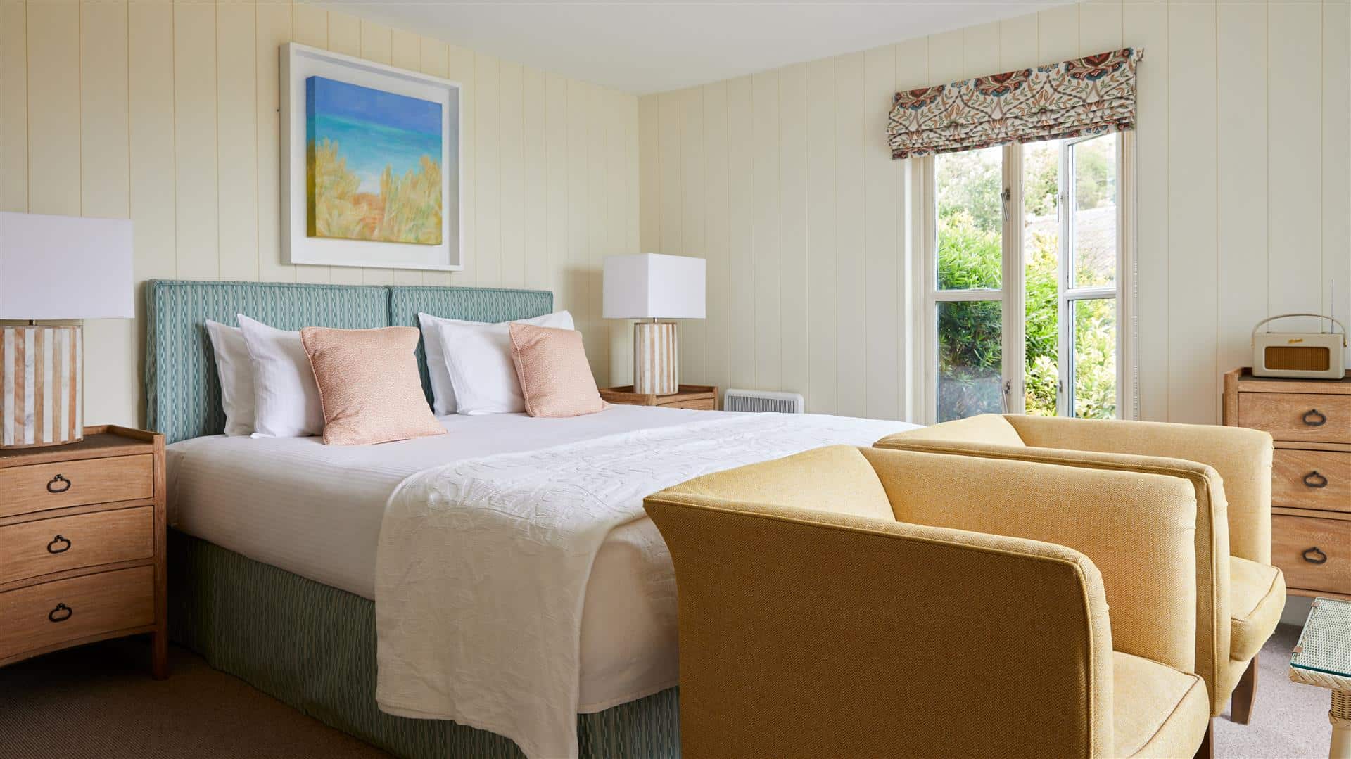 Hotel bedroom with king size bed, two armchairs, a Roberts Radio, neutral décor and seaside artwork
