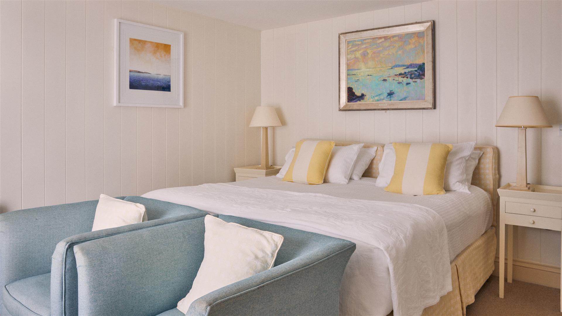 Hotel room with king size bed, two armchairs and neutral decor with seaside artwork on the walls